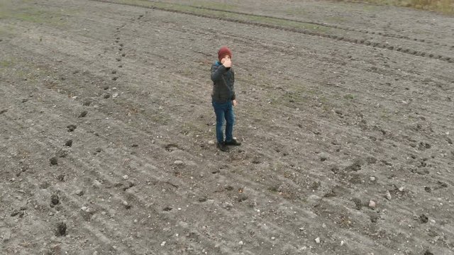 The lonely boy wanders in autumn in an empty, plowed, gray field. The croaker is looking for something in the field. The boy is running and walking.