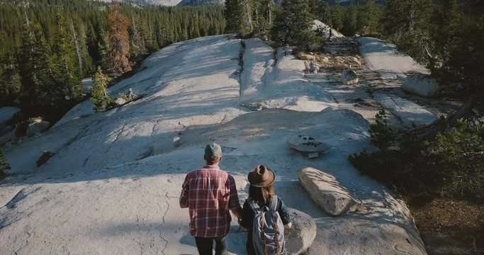 Drone camera follows young romantic couple hiking together along amazing white rock at Yosemite national park forest.