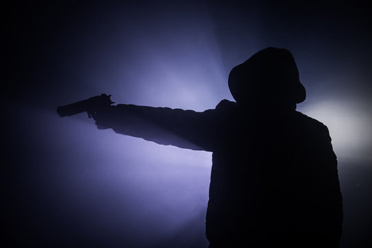 Silhouette of man with assault rifle ready to attack on dark toned foggy background or dangerous bandit in black wearing balaclava and holding gun in hand. Shooting terrorist with weapon theme decor