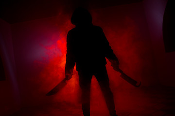 A dangerous hooded man standing in the dark and holding a knife. Face can not be seen. Committing a crime concept. Selective focus