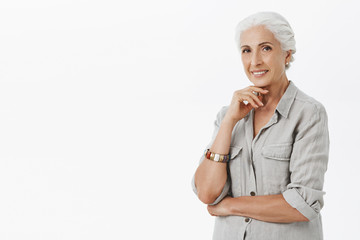 Waist-up shot of charming old lady with grey hair in casual shirt and bracelet holding finger above...