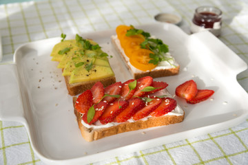 Breakfast: Toast with strawberries, avocado and yellow cherry tomatoes on a plate, top view