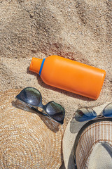 Male and female sunglasses,  sunhats and a sunprotection cream at the sand as a reminder of protection importance during the sun exposure.