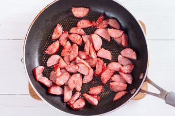 Step-by-step cooking pasta with sausage in tomato sauce and cheese, step 3 - sausage frying, selective focus, top view