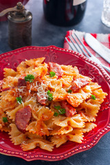 Pasta - bows with smoked sausage and cheese in a red plate, selective focus