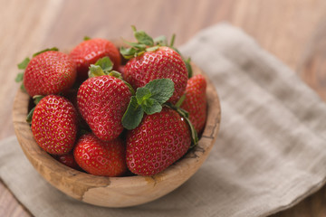 Ripe strawberries in wooden bowl on wood background with copy space