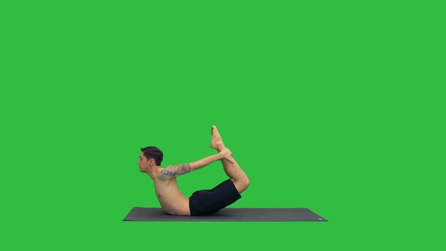 Sporty muscular young yogi man doing backbend exercise, dhanurasana, Bow Posture on a Green Screen, Chroma Key.