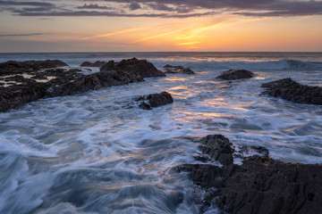 Fototapeta na wymiar Westward Ho! seascape sunset with waves crashing around the rocks with golden sky