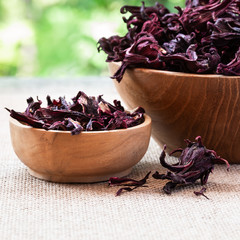Hibiscus (Roselle, karkade) dry flowers in wooden bowles on burlap and green natural background.