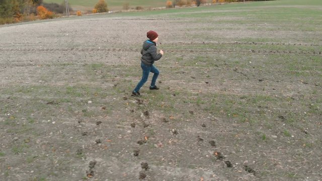 The lonely boy wanders in autumn in an empty, plowed, gray field. The croaker is looking for something in the field. The boy is running and walking.