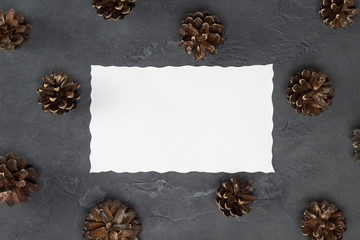 White paper and pine cones on gray concrete background. Card, forest, winter, Christmas, New Year concept. Top view, flat lay, copy space, mock up