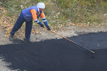 Female worker during asphalting road. Heavy female manual labor in construction