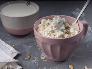 Light breakfast of cottage cheese and sour cream in pink dishes, teaspoons on a gray background, linen napkin, close-up