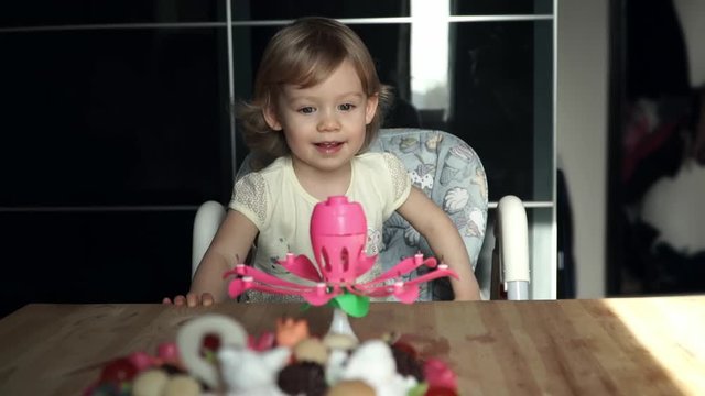Little cute girl sitting in front of the cake, blows out the candles on her birthday and smiles
