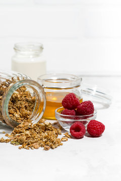 sweet granola in a jar, fresh raspberries and honey on white table, vertical closeup