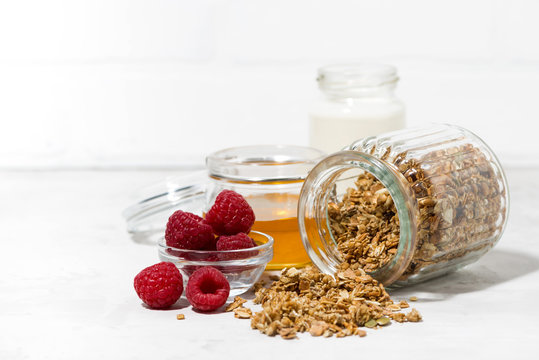 sweet granola in a jar, fresh raspberries and honey on white table