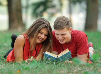 couple of students lying on the grass in the Park and reading a book