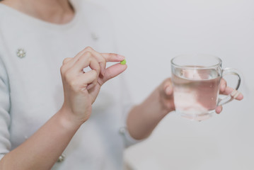 Woman holding pill and glass of water in hands taking emergency medicine, supplements or antibiotic antidepressant painkiller medication to relieve pain, meds side effects concept, close up view