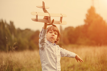 Child pilot aviator with plane at sunset, little boy playing with cardboard toy airplane outdoors,...