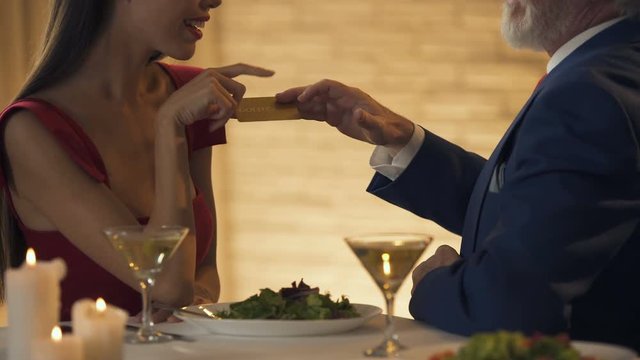 Young lady giving air kiss to her old sponsor in exchange for golden card, money
