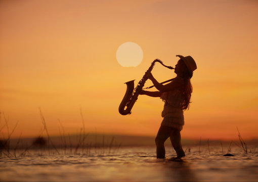 Woman playing saxophone on water with sunset background