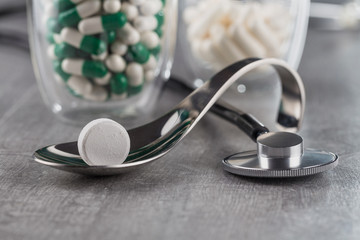 close-up of a large white tablet on a metal spoon on background a stethoscope and medication