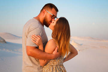 lovely attractive couple kissing on the white sand beach or in the desert or in the sand dunes, happy couple embracing at the beach on a sunny day, couple in love