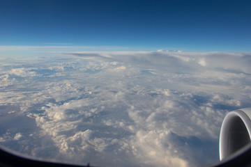 View from the airplane porthole. Blue sky in the horizon and white clouds below. Jet engine...