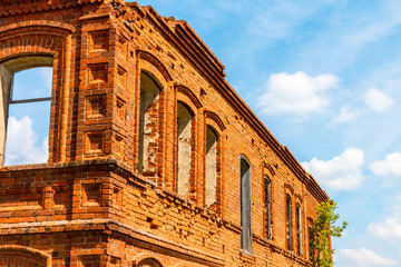 Fototapeta premium A large ruined ancient house of red brick against a blue sky with white clouds.