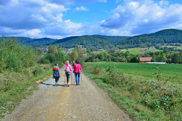 Group of tourist, hikers and backpackers are waling on the country road. Beautiful nature around them. 
Outdoor activity and walking in the countryside. Wysowa, Low Beskids (Beskid Niski), Poland