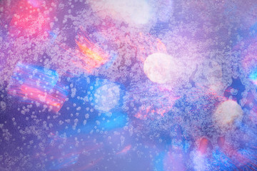 Fototapeta premium Winter background in soft pastel colors. Frost and snowflakes on the window. Multicolored bokeh with blur. Glare through glass. Background for holiday greetings with winter theme.