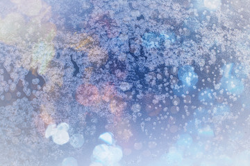Winter background in soft pastel colors. Frost and snowflakes on the window. Multicolored bokeh with blur. Glare through glass. Background for holiday greetings with winter theme.