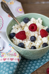 Cottage cheese in bowl with raspberries and blueberries on wooden background. Healthy breakfast .Place under the text