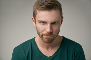 angry sullen young man in a t-shirt looks hard at the camera and frown. the concept of bad mood failure disorder. large Studio portrait on isolated background