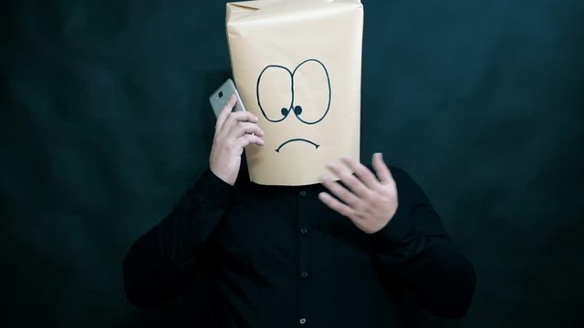Emotion concept. A young man listens to information on a mobile phone. With his left hand he gestures in protest, pointing down with his thumb. On the face expressed sadness.