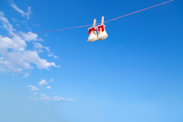 青空に木製洗濯挟みで吊るされた赤いリボンの新生児用靴下。赤ちゃん、育児、出産、幸せ、愛イメージ