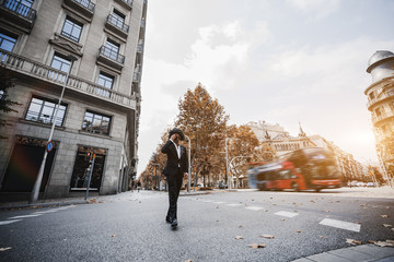 Wide-angle view of a stylish young businessman in the sunglasses and with curly hair, he is...