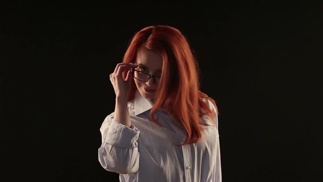 a beautiful girl with red hair in a white shirt posing on a black background in front of the camera. the model advertises glasses, lenses or services to restore vision