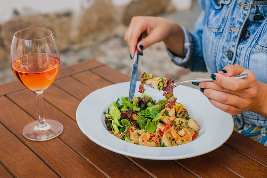 Girl, eating salad with shrimps, drinking a glass of rose wine