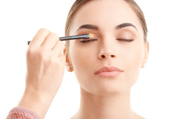 Fototapeta premium Make-up eyes. Studio shot of a beautiful young woman having a makeup brush on her eyes against at isolated white background. 