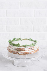 Cake on glass stand decorated with sprigs of rosemary