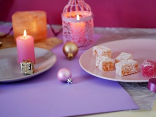  Decorative composition in a pink color from burning candles, decorative lanterns, oriental sweets on dishes, Christmas decor, balls on a light silver background, romantic atmosphere, seasonal winter 