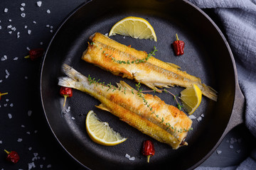 Top view of fried smelts on frying pan with lemon