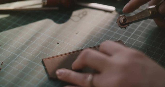 Close-up shot of female hands working, cutting edge and marking holes on piece of leather with professional hand tools.