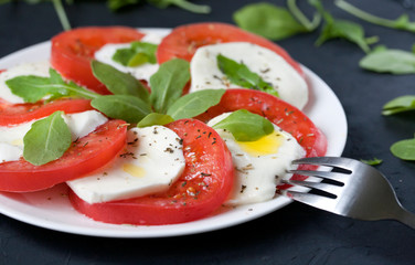 Tomato and mozzarella salad with lettuce on a white plate with fork.