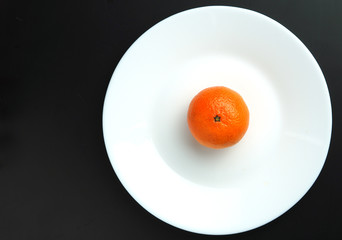 ripe tangerines in a white plate on a black background