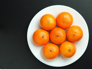 ripe tangerines in a white plate on a black background