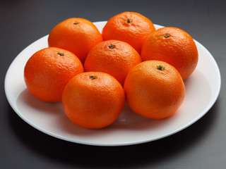 ripe tangerines in a white plate on a black background