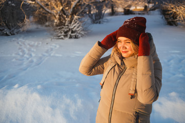 Pretty young woman in red mittens and red winter hat enjoying good sunny winter day in snowy nature