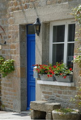 Fototapeta na wymiar Ville de Genêts, maison en pierre, porte bleue et fleurs au bord de la fenêtre, banc en pierre, département de la Manche, France 